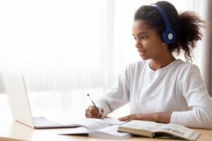 African American teen girl wearing headphones learning language online African American teen girl wearing headphones learning language online